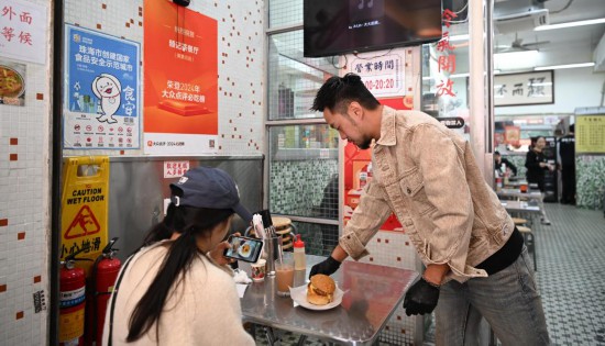 12月13日，邱志暉（右）在其創(chuàng)辦的茶餐廳珠海夏灣店里給顧客送餐。新華社記者 鄧華 攝