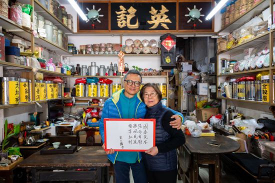 12月18日，澳門英記茶莊的傳承人盧石麟（左）與夫人在展示祝福語(yǔ)。